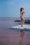 A beautiful woman in a seductive blue bikini stands on a wooden raft covered in salt. The salt lake is pink. Deposit and