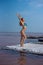 A beautiful woman in a seductive blue bikini stands on a wooden raft covered in salt. The salt lake is pink. Deposit and