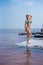 A beautiful woman in a seductive blue bikini stands on a wooden raft covered in salt. The salt lake is pink. Deposit and