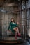 Beautiful woman sitting in a cage alone because of her limitations and complexes. adult female wearing green evening dress inside