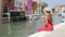 Beautiful woman sitting on the edge of the canal of Burano, Venice, Italy. Slow motion.