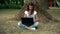 Beautiful woman sitting on the grass near the tree with a laptop