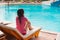 Beautiful woman sitting on a lounger pool background