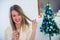 Beautiful woman sitting next to Christmas tree enjoying glass of