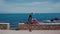 Beautiful woman sitting on the stone fence above town Antibes in South France, enjoying beautiful sea view. Distant plan