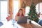 Beautiful woman sitting at the table working with laptop at home around christmas tree smiling pointing to head with both hands