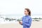 Beautiful woman standing on beach holding phone with earphones