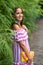 A beautiful woman in a striped dress and with a handbag in her hands ,stands near a lush, green grass fence