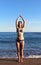Beautiful woman in swimsuit makes yoga on beach near blue sea