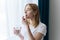 Beautiful woman takes a pill near the window with a glass of water. Beautiful smiling woman taking vitamin tablet. Food