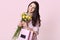 Beautiful woman with toothy smile, has long dark straight hair, tilts head, carries bouquet of flowers and bag with present, poses