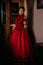 Beautiful woman in vintage 1800s early 1900s clothing red dress in old interior. Historical dresses, vintage outfits