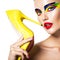 Beautiful woman with vivid make-up of eyes holds the yellow high heel