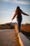 Beautiful woman walking and balancing on street curb or curbstone during sunset