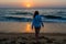 Beautiful woman walking on the beach towards ocean during sunset time