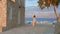 Beautiful woman walks on sidewalk, stops to enjoy amazing sea view. Resort town