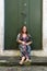 Beautiful woman wearing African clothing sitting on the edge of a green colored door. Quiet and happy person