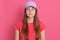 Beautiful woman wearing baseball cap and t shirt posing isolated over pink background, looks at camera with serious expression on