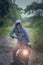 beautiful woman wearing blue jeans jacket sitting on enduro motorcycle against colorful natural background