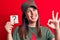 Beautiful woman wearing cap with red star communist symbol holding question mark reminder doing ok sign with fingers, smiling