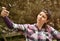 Beautiful woman wearing checked shirt and baseball cap taking selfie in the city park.