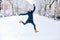 Beautiful woman wearing in jeans, blue down jacket, knitted hat and yellow boots jumping in snow outdoors