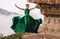 Beautiful woman wearing long green dress dancing on the edge of a cliff. Mezmay.