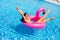 Beautiful woman, wearing swimsuit, lying on a pink flamingo air mattress in a pool of blue water, summer