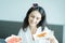 A beautiful woman wearing a towel and a white bathrobe has to eat a pizza and sliced tomato with happy and relaxing on the bed at