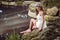 Beautiful woman wearing white dress sitting on the rock near a lake