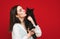 Beautiful woman in white shirt hugs and kisses black cat on red background. A woman loves her pet. Portrait of a girl with a cat