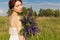 Beautiful woman in white sundress with a bouquet in the hands of lupine in field at sunset