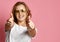 Beautiful woman in white t-shirt and aviator sunglasses show thumbs up sign on pink