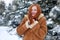 Beautiful woman on winter outdoor, snowy fir trees in forest, long red hair, wearing a sheepskin coat