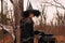 Beautiful woman in witches hat and costume holding broom near the cauldron in autumn forest. Halloween concept