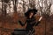 Beautiful woman in witches hat and costume preparing a potion in cauldron in autumn forest. Halloween concept. Selective