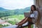 A beautiful woman working and typing on laptop computer while sitting on balcony with mountains and green nature background