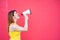 Beautiful woman in a yellow dress shouts in a megaphone on a red background. Stylish red-haired lady in sunglasses