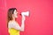 Beautiful woman in a yellow dress shouts in a megaphone on a red background. Stylish red-haired lady in sunglasses