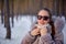 Beautiful womanin winter forest wearing a fur coat and sunglasses. It is snowing. She is happy in winter. Smiling