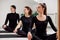 Beautiful women are doing Pilates in a bright studio. Three female athletes in black suits sit cross-legged on yoga mats