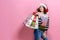 Beautiful women wearing bright Christmas carrying colorful shopping bags. On pink background. Christmas shopping And