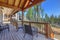 Beautiful wooden back porch with chairs on the hill and large backyard patio with fire pit and pine trees