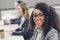 Beautiful young african american woman in headset smiling at camera while working with colleagues