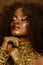 Beautiful young African woman with gold earthy makeup and necklace, laying hands on her chin eyes closed, brown background