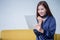 Beautiful young asian woman excited looking at digital tablet computer smiling girl with touch pad on yellow sofa