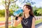 Beautiful young Asian woman exercising in the morning at a running track, taking a rest to drink water