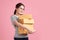 Beautiful Young Asian woman holding parcel box isolated on pink background, Delivery courier and shipping service concept