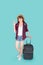 Beautiful young asian woman pulling suitcase isolated on blue background, asia girl cheerful holding luggage