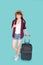 Beautiful young asian woman pulling suitcase isolated on blue background, asia girl cheerful holding luggage walking
